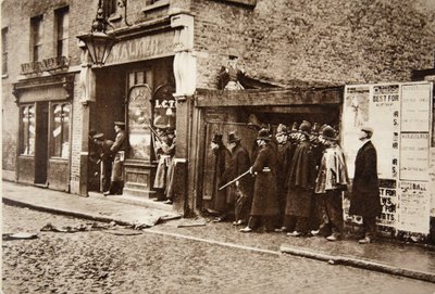 Peeping round corners, he exposed himself with the Scots Guards to the random fire of the besieged burglars: Mr. Winston Churchill top-hatted in the East End of London, during the Sidney Street Drama by English Photographer